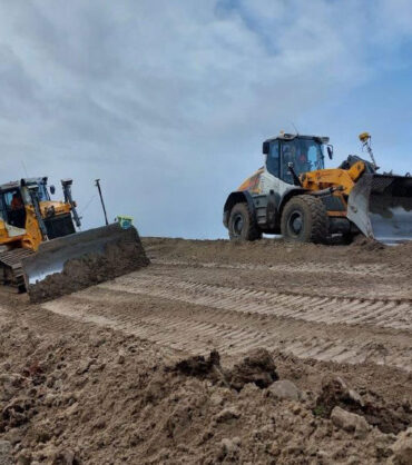 Een zandpad met daarop een mobiel en een rupsgraafmachine