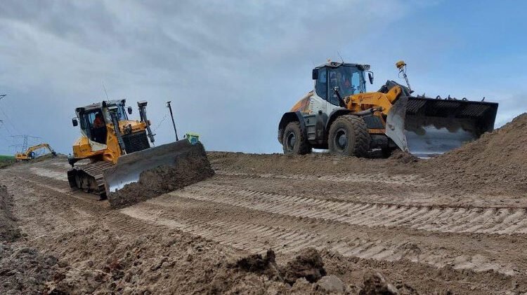Een zandpad met daarop een mobiel en een rupsgraafmachine