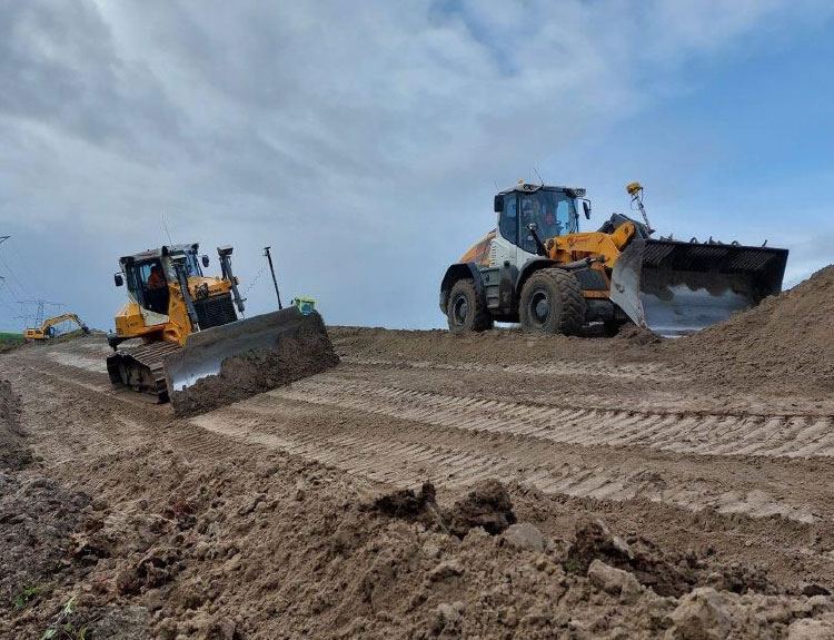 Een zandpad met daarop een mobiel en een rupsgraafmachine
